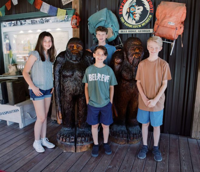 children standing next to carved statues of Bigfoot