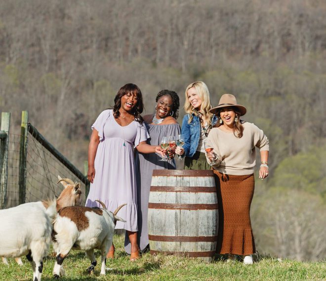 Women enjoying wine outdoors next to some playful goats