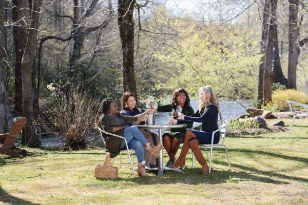 a group of women drinking wine and eating outdoors by a river