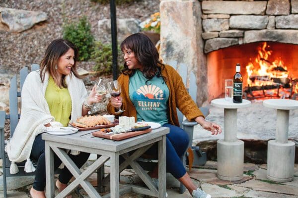 women drinking wine and snacking next to a fire outdoors