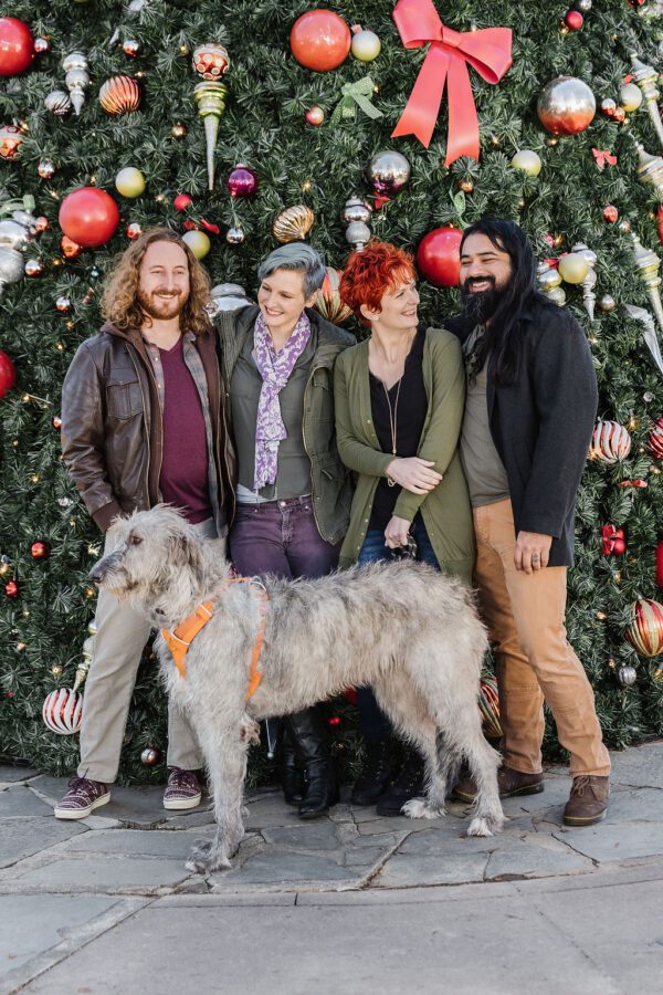 friends and their dog by a large christmas tree