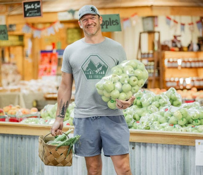 a man holding a bag of fresh apples and corn