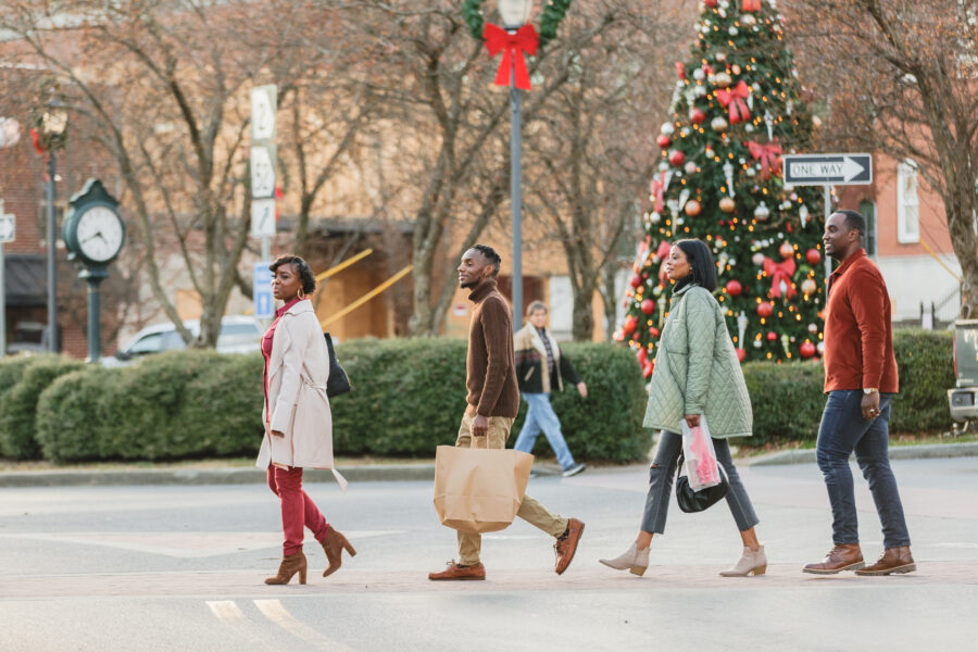 Two Couples walking across River Street with shopping bags and a Christmas tree in the background